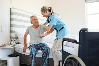 caregiver helping a senior man get up from a bed
