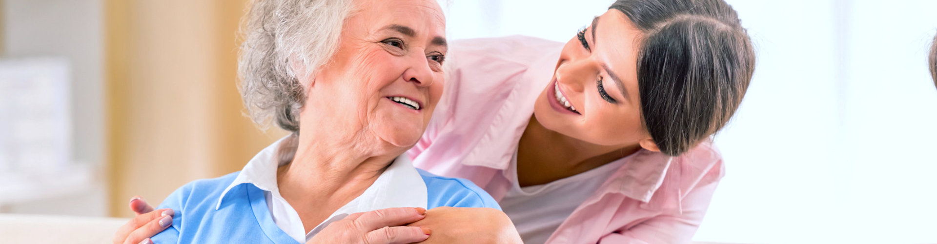 caregiver smiling with her senior patient from behind